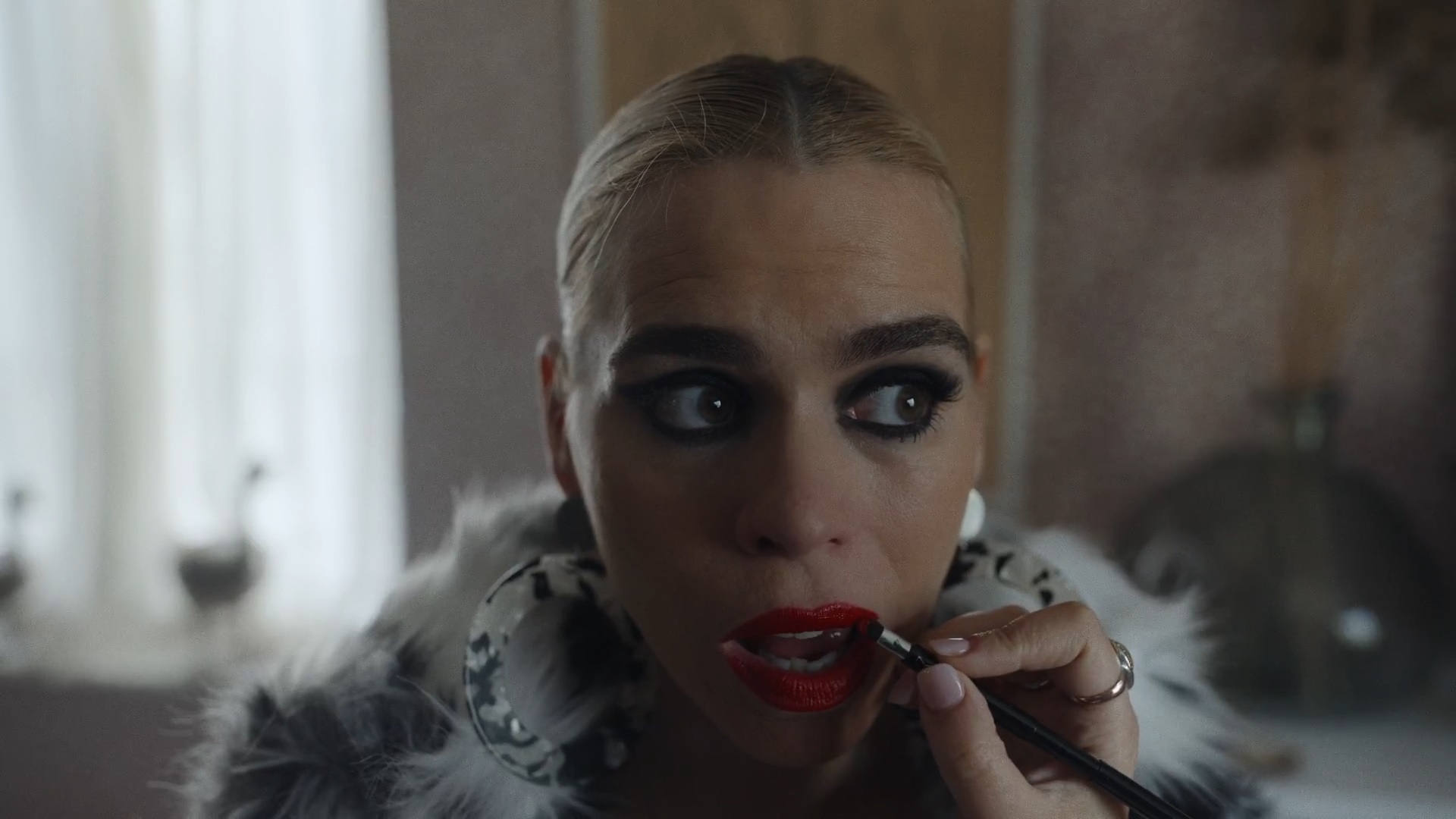 I Hate Suzie. A close up of protagonist Suzie (Billie Piper), wearing heavy makeup and a fluffy black and white coat. She is leaning forward towards the camera as someone applies her bright red lipstick.